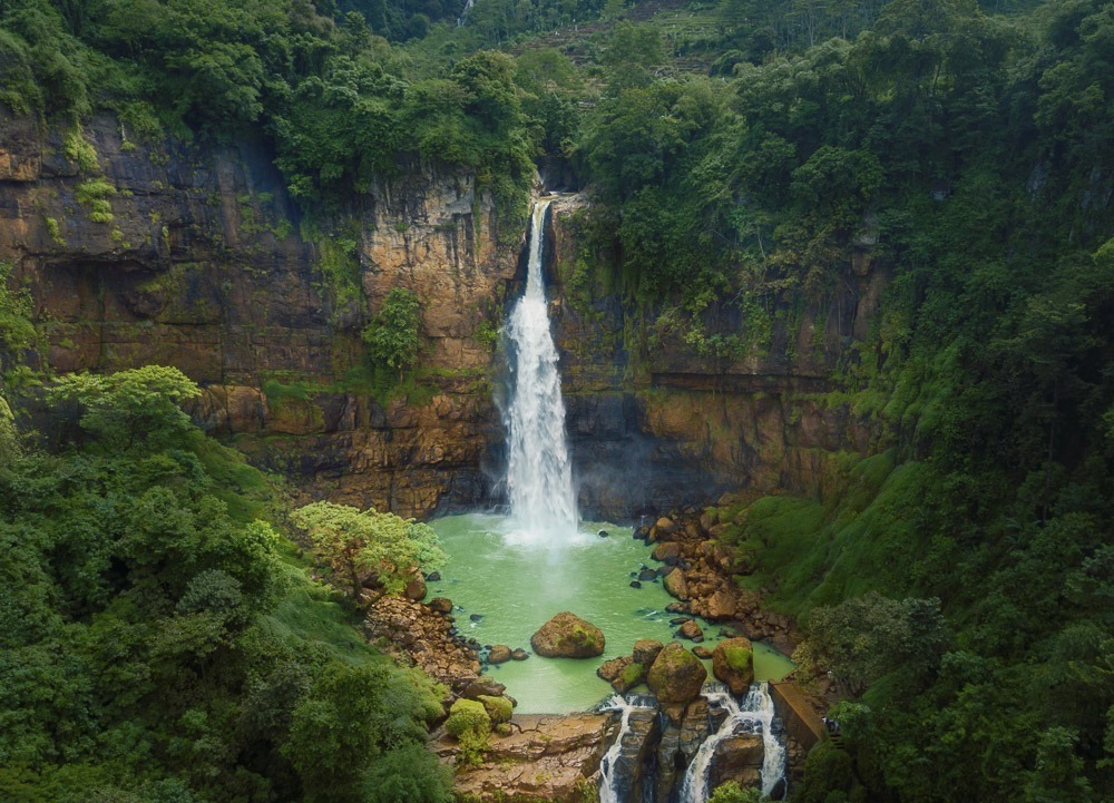 Cachoeira Gitgit em Bali, cercada por vegetação densa e pedras em uma lagoa de águas verde-esmeralda.