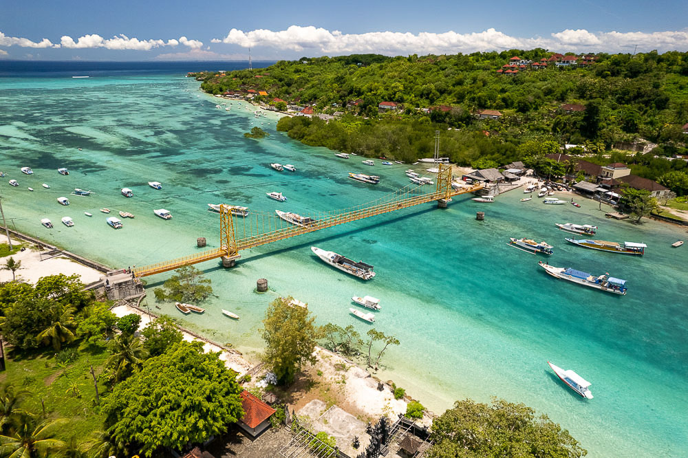 Ponte amarela conectando Nusa Lembongan a Nusa Ceningan, cercada por águas azul-turquesa e barcos ancorados.