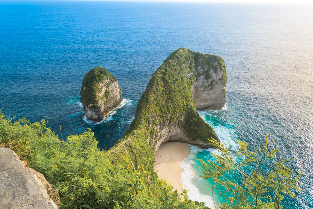 Vista panorâmica da Kelingking Beach em Nusa Penida, Bali, com um penhasco verde em formato de tiranossauro cercado pelo oceano azul profundo.