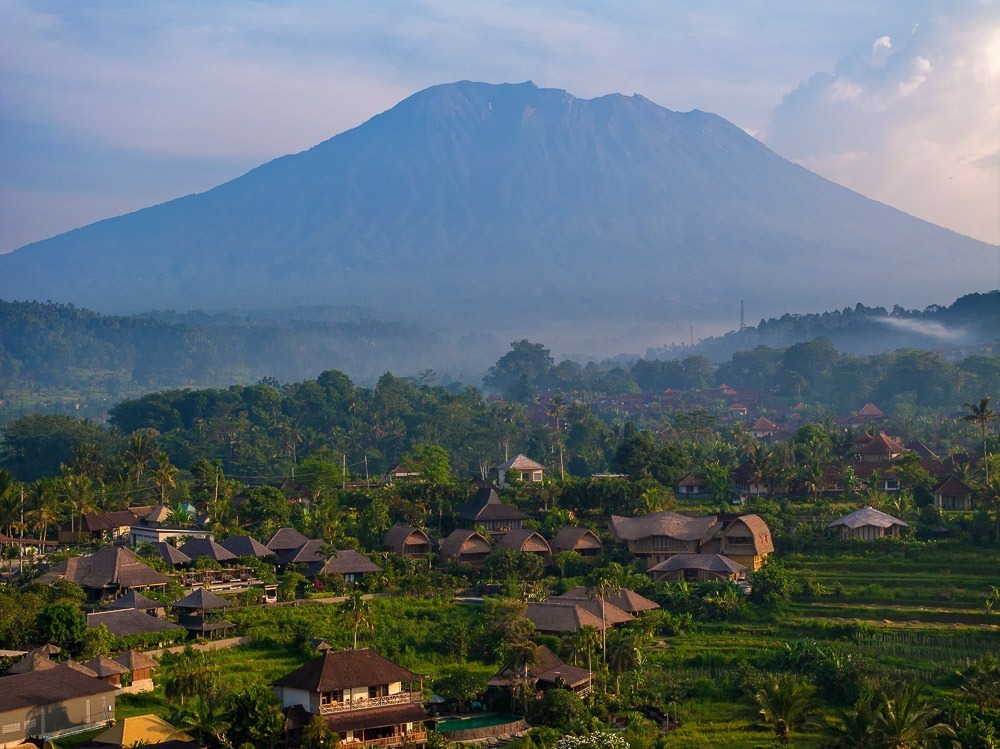 Paisagem de Sidemen em Bali, com casas tradicionais cercadas por arrozais verdes exuberantes e o Monte Agung ao fundo.