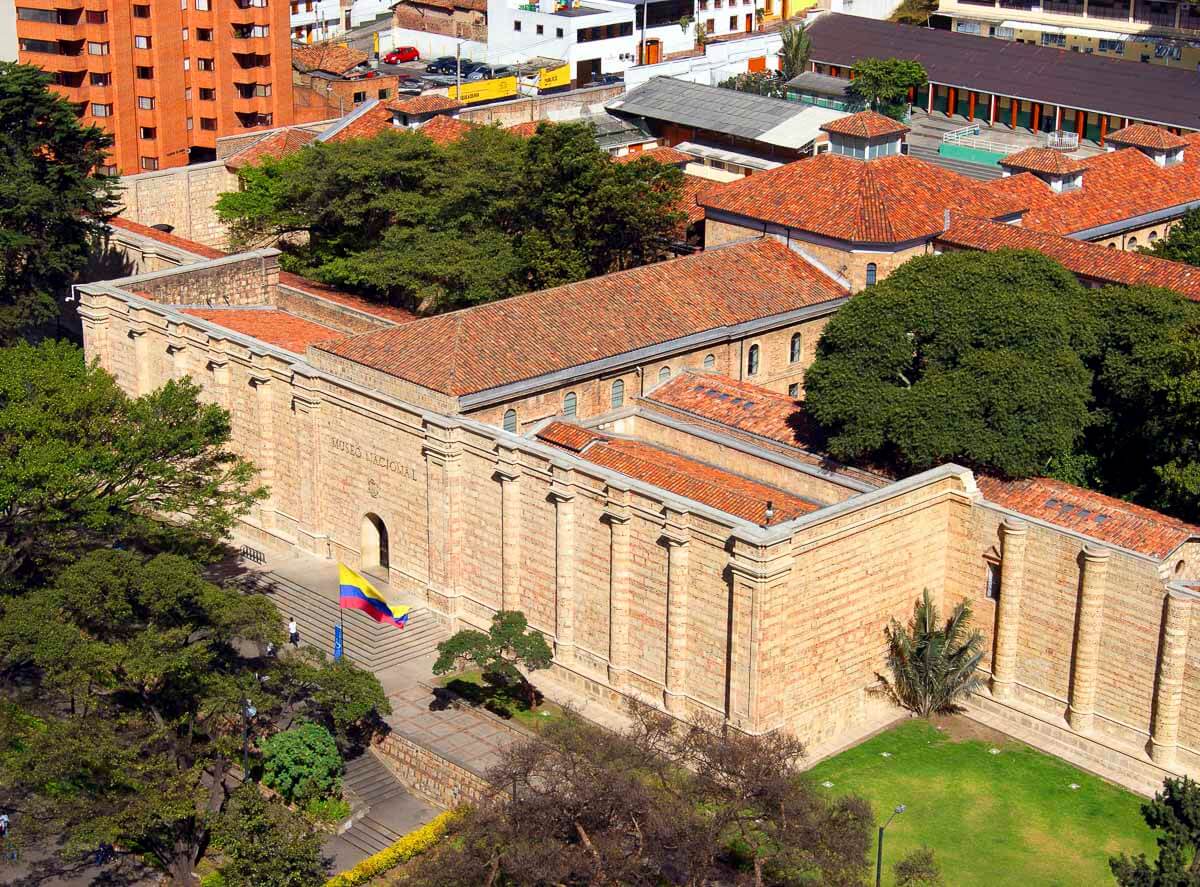 Vista aérea do bairro Santa Fé em Bogotá, com construções de telhados avermelhados e o Museu Nacional ao centro, rodeado por árvores e bandeira da Colômbia hasteada.