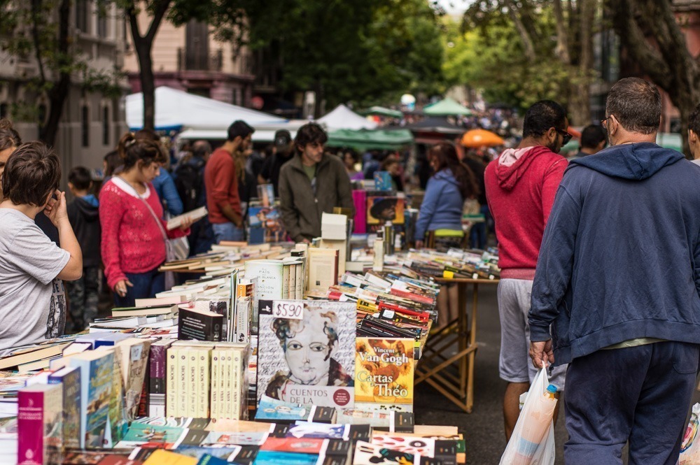 Feira de rua movimentada em Montevidéu, com diversas barracas vendendo livros e um público variado explorando os produtos.