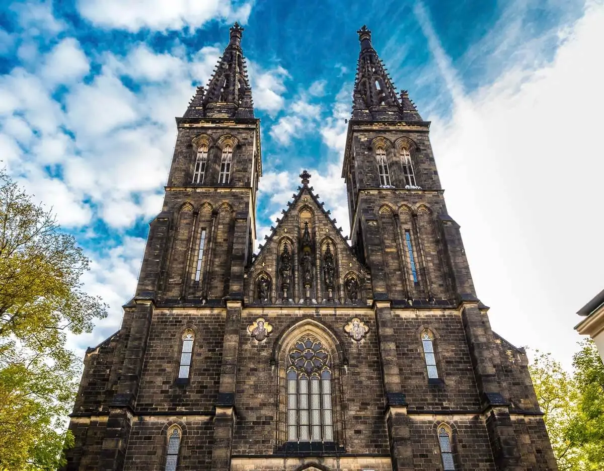 Fachada frontal da Catedral de São Pedro e São Paulo em Vyšehrad, com torres góticas e céu azul ao fundo.