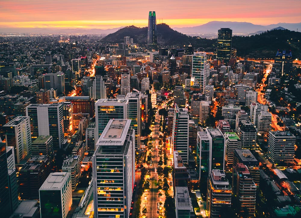 Vista panorâmica de Santiago ao entardecer, com a Torre Costanera e luzes da cidade se acendendo.