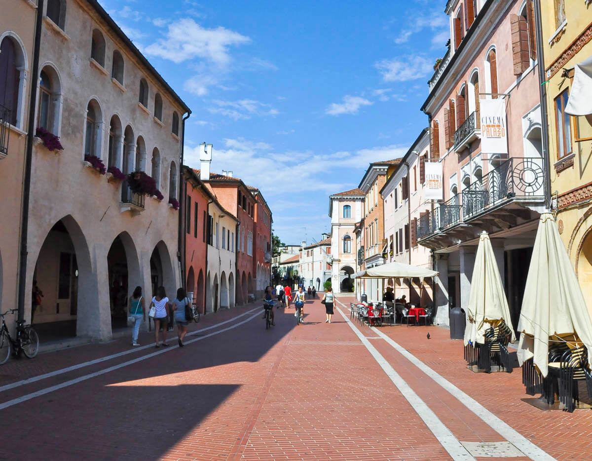 Rua de Mestre, na Veneza Continental, com edifícios históricos, restaurantes ao ar livre e pedestres passeando sob o céu azul.