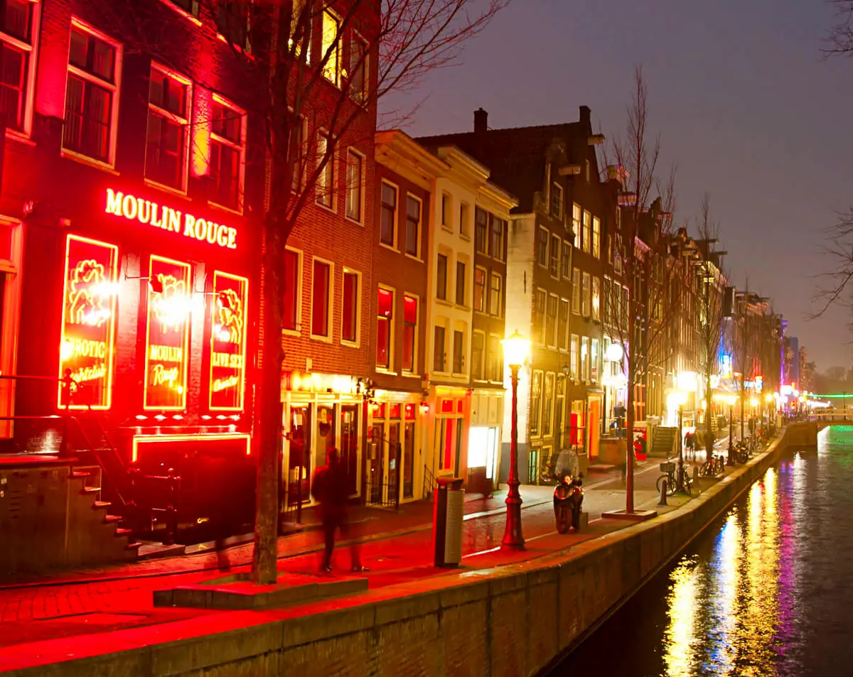 Fachada iluminada do Moulin Rouge em De Wallen, o famoso Bairro da Luz Vermelha de Amsterdam, com reflexos das luzes vermelhas no canal.