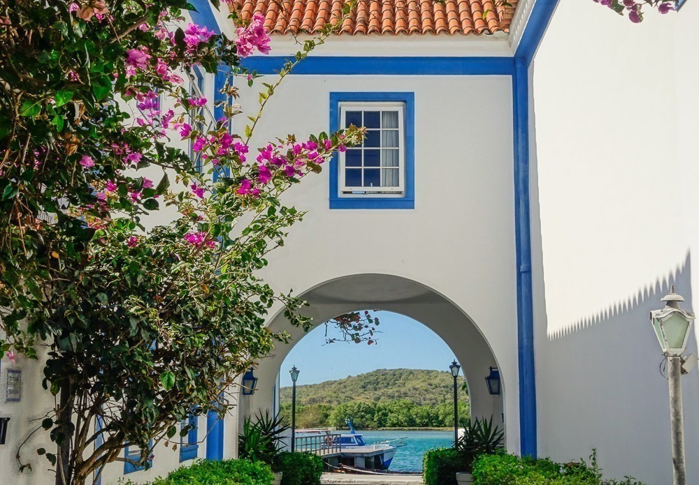 Arco azul e branco em estilo colonial no Bairro da Passagem, em Cabo Frio, com uma lancha azul no canal ao fundo.