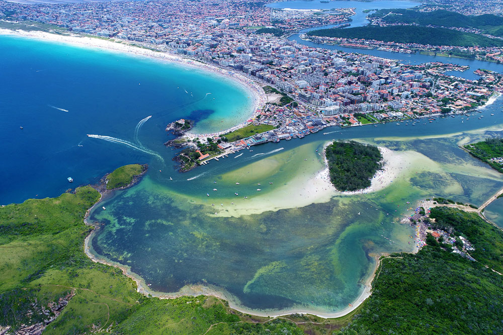 Vista aérea de Cabo Frio, mostrando praias de águas azuis, ilhas e a cidade ao fundo.