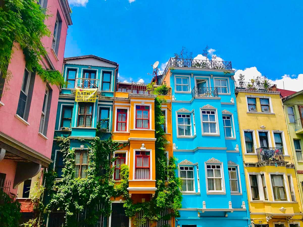 Fachada de prédios coloridos no bairro de Balat, em Istambul, com arquitetura otomana tradicional e detalhes verdes de vegetação subindo pelas paredes.