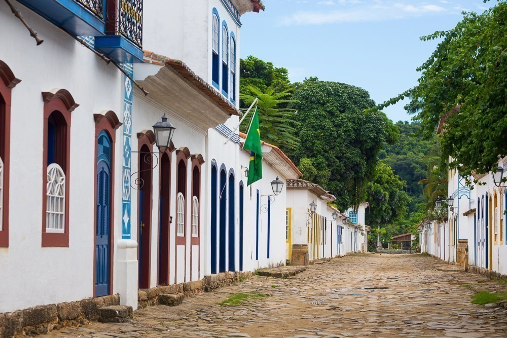 Rua de paralelepípedos no Centro Histórico de Paraty, cercada por casas coloniais brancas com janelas e portas coloridas.
