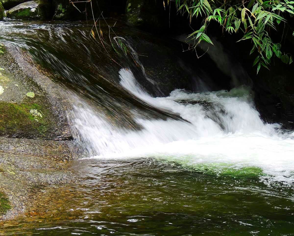 Queda d’água entre pedras e vegetação, em meio à natureza exuberante de Penedo.