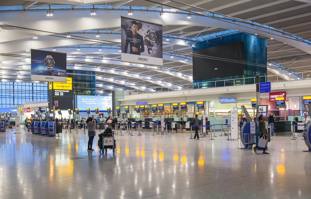 Saguão do Aeroporto de Heathrow em Londres, com guichês de check-in iluminados, sinalização em inglês e poucas pessoas circulando.