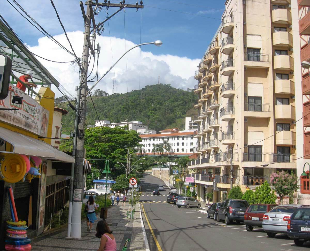 Rua movimentada próxima ao centro de Águas de Lindóia, com calçadas largas, lojas e hotéis ao fundo.
