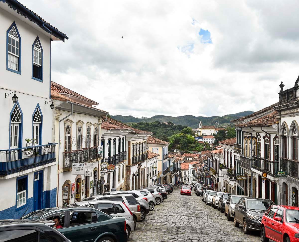 Rua em declive no centro histórico de Ouro Preto, ladeada por casarões coloniais coloridos e carros estacionados.