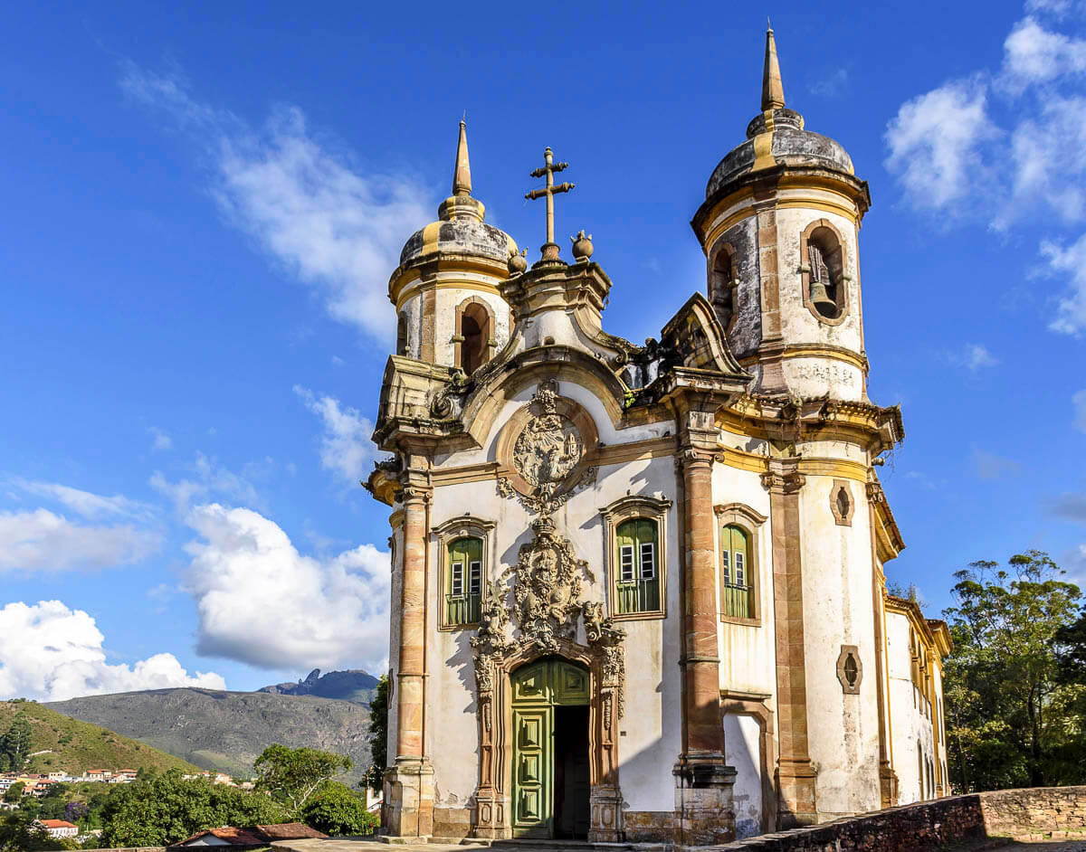 Fachada barroca da Igreja de São Francisco de Assis em Ouro Preto com céu azul ao fundo.