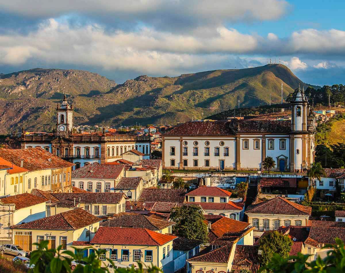 Vista panorâmica do centro histórico de Ouro Preto com prédios coloniais, igreja e montanhas ao fundo.