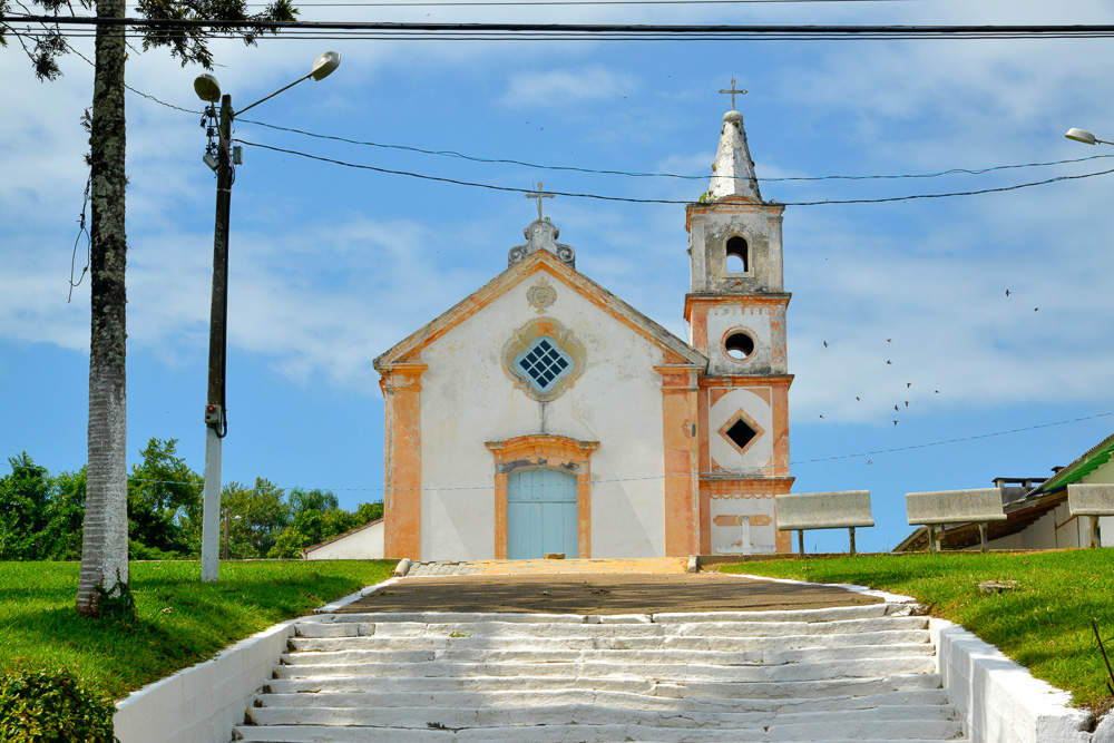 Capela de São João Batista em Penha com fachada branca, detalhes em tom salmão e escadaria central.
