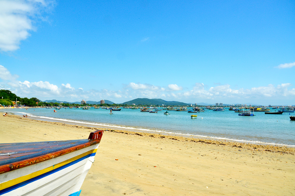 Praia da Armação com areia dourada, barcos no mar e montanhas ao fundo.