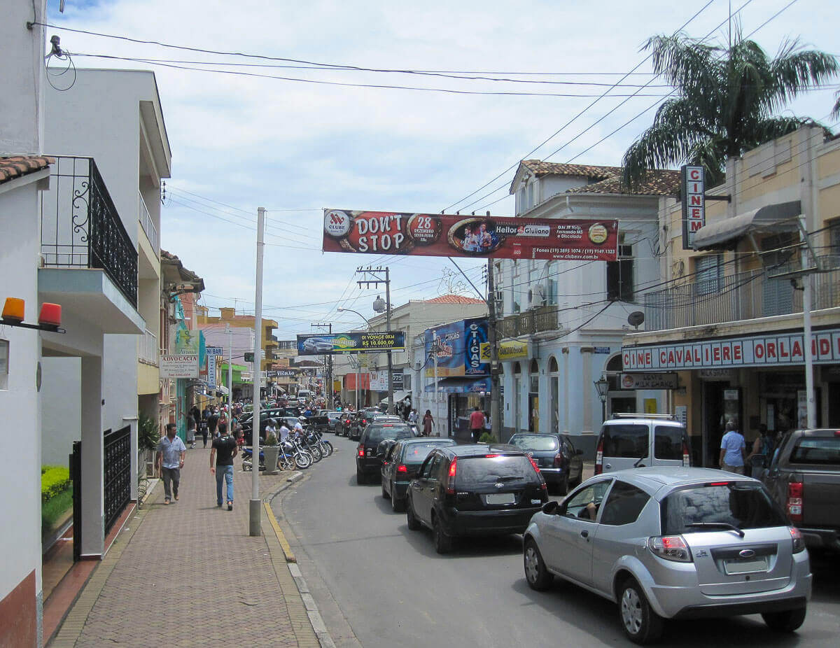 Rua movimentada no centro de Socorro, SP, com lojas, carros e pedestres.