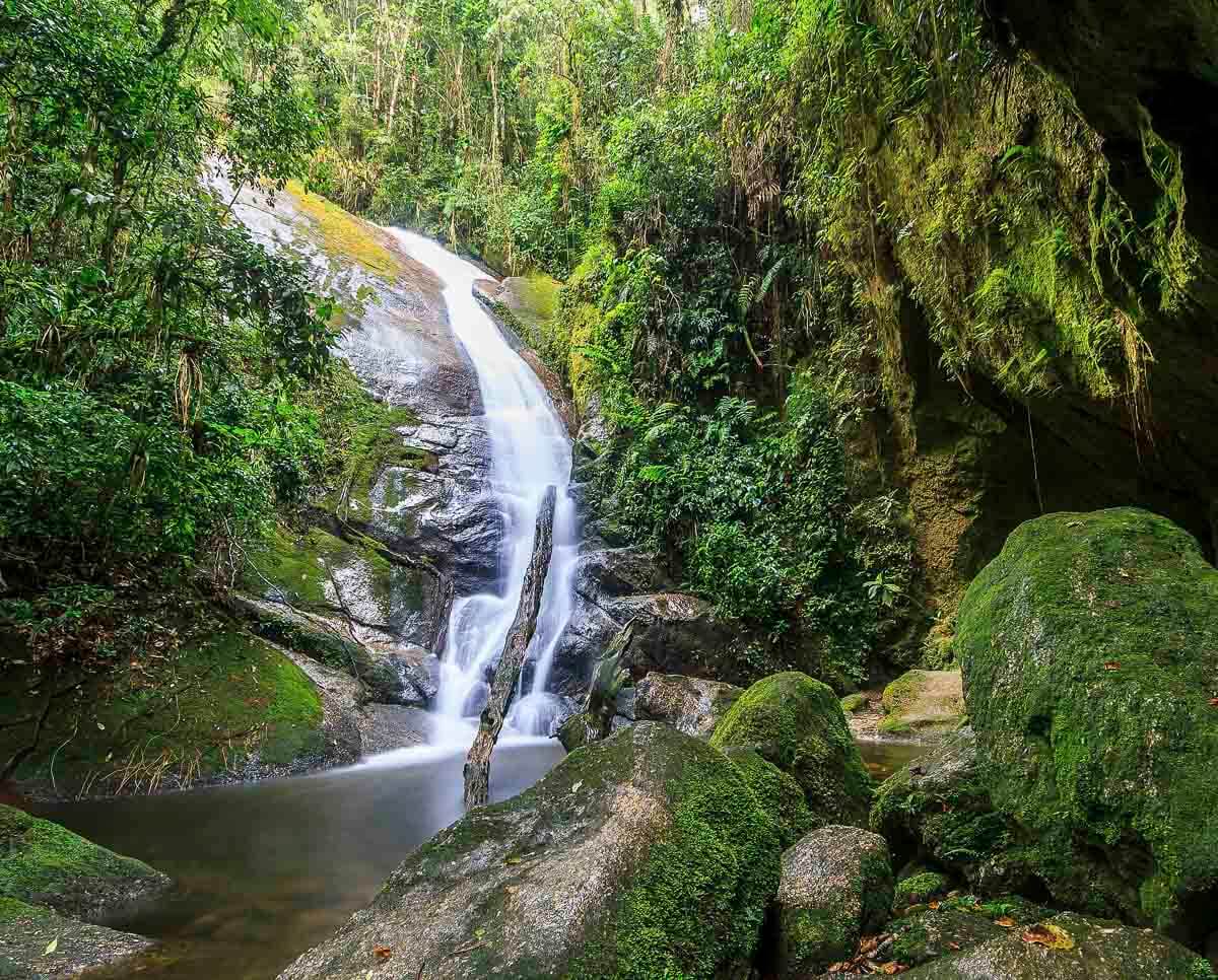 Cachoeira Gruta do Granito, com queda d’água fina e alta escorrendo por rocha inclinada em meio à mata fechada.