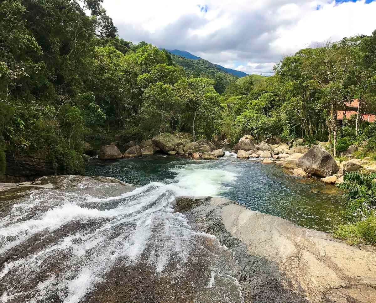 Vista superior da Cachoeira do Escorrega em Visconde de Mauá, com água escorrendo por uma rocha lisa até um poço natural.