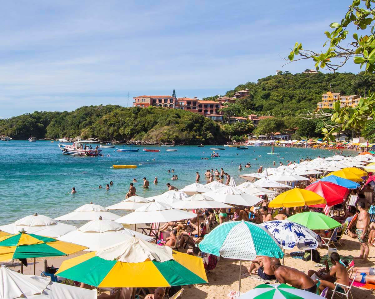 Praia de João Fernandes em Búzios com mar calmo e transparente, repleta de guarda-sóis coloridos e turistas.