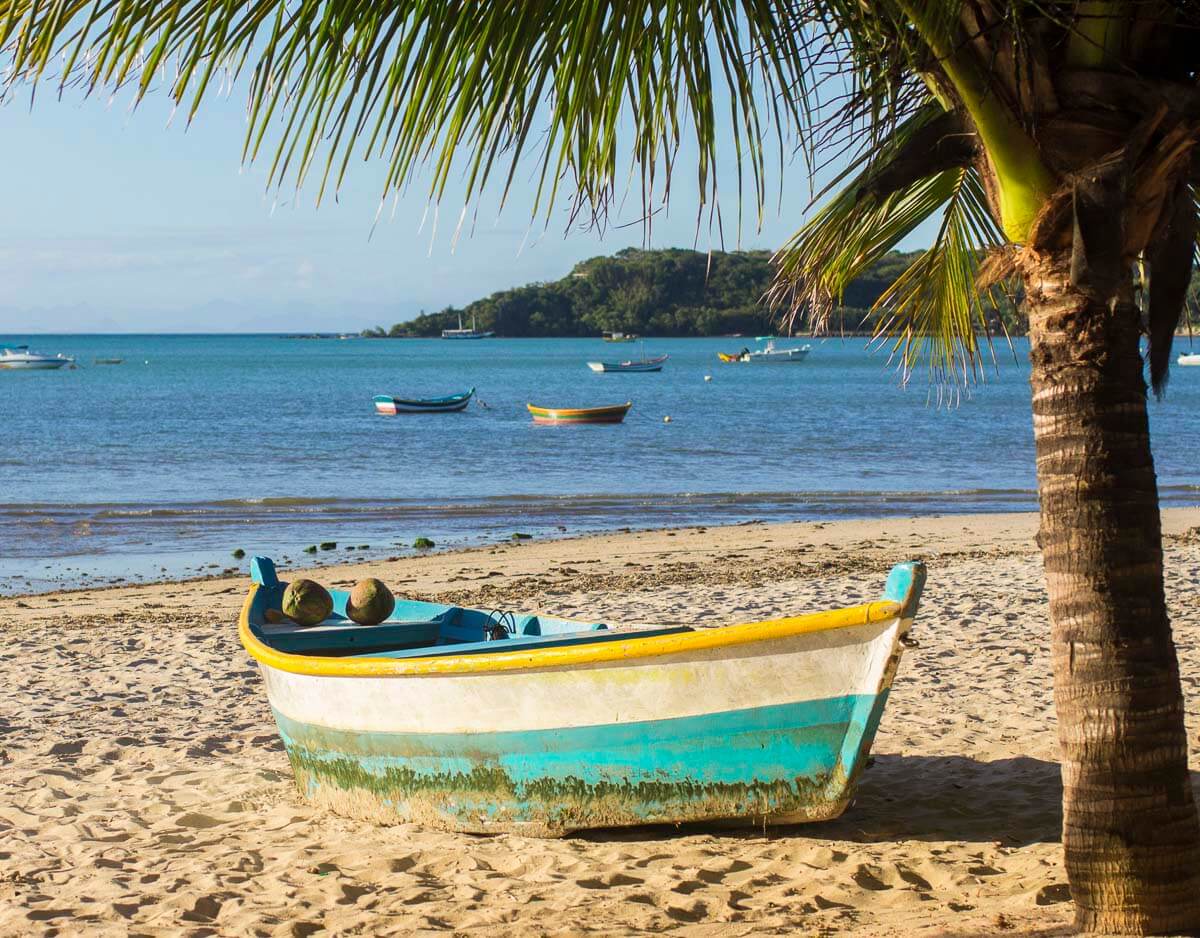 Barco de pescador encostado na areia da Praia de Manguinhos, com vista para o mar calmo e coqueiros.