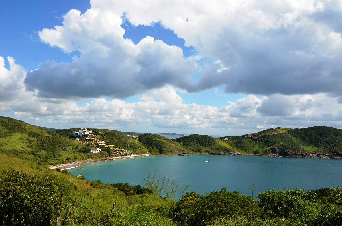Vista panorâmica da Praia Brava em Búzios, com morros verdes e mar azul formando uma enseada isolada.