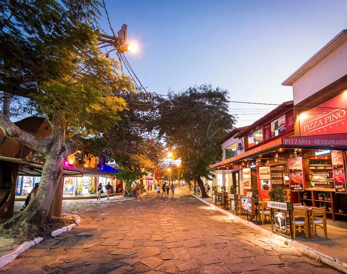 Rua das Pedras em Búzios ao entardecer, com lojas iluminadas, restaurantes e pedestres passeando.