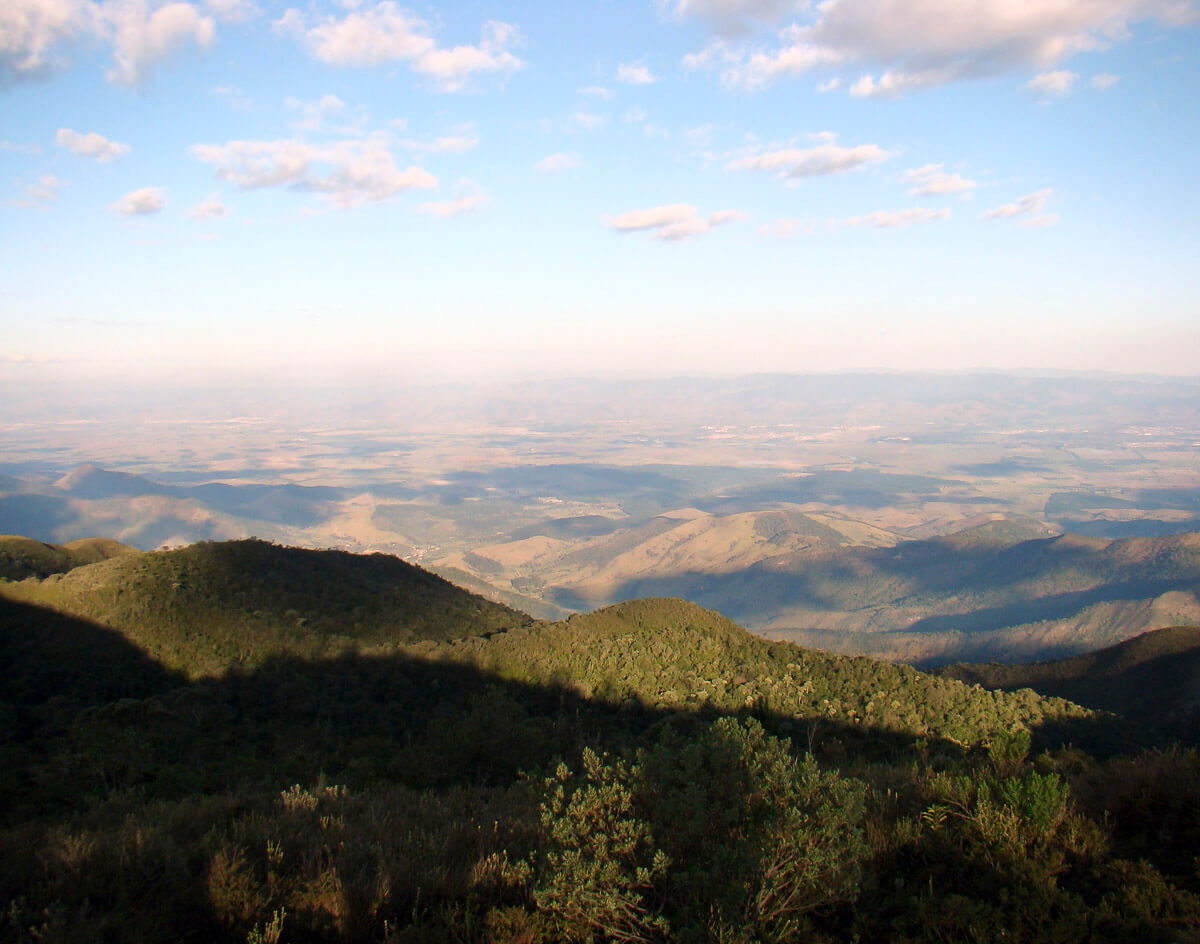 Vista ampla do Pico do Itapeva com vales e montanhas ao fundo sob céu azul.