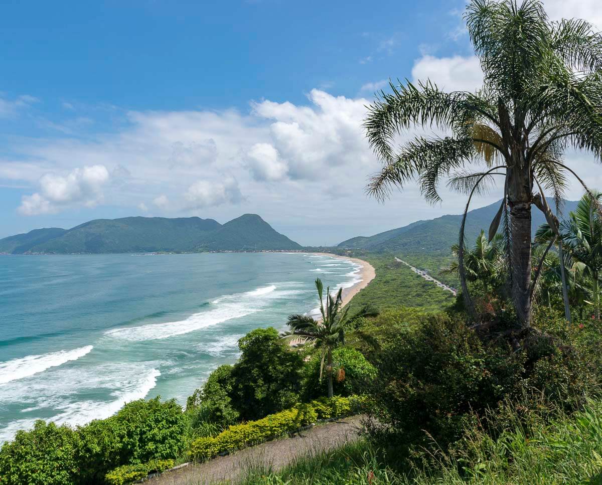 Vista panorâmica da Praia da Armação cercada por morros verdes e vegetação tropical.