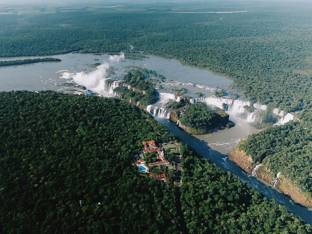 Vista aérea do Belmond Hotel das Cataratas em meio à floresta, próximo às quedas d'água.
