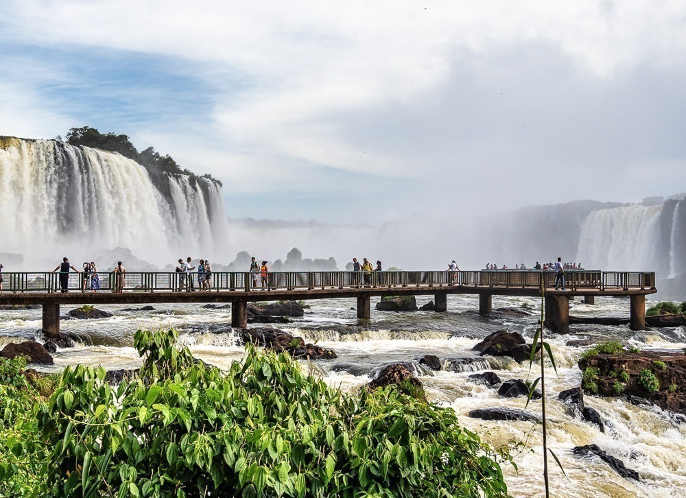 Passarela com turistas em frente às Cataratas do Iguaçu em um dia nublado.
