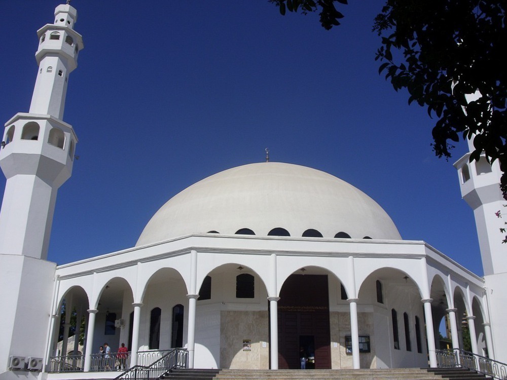 Mesquita branca de Foz do Iguaçu com cúpula central e duas torres laterais sob céu azul intenso.