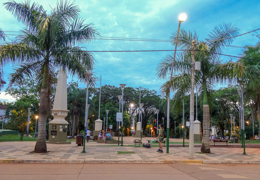 Praça San Martín em Puerto Iguazú, com palmeiras e monumento ao centro.