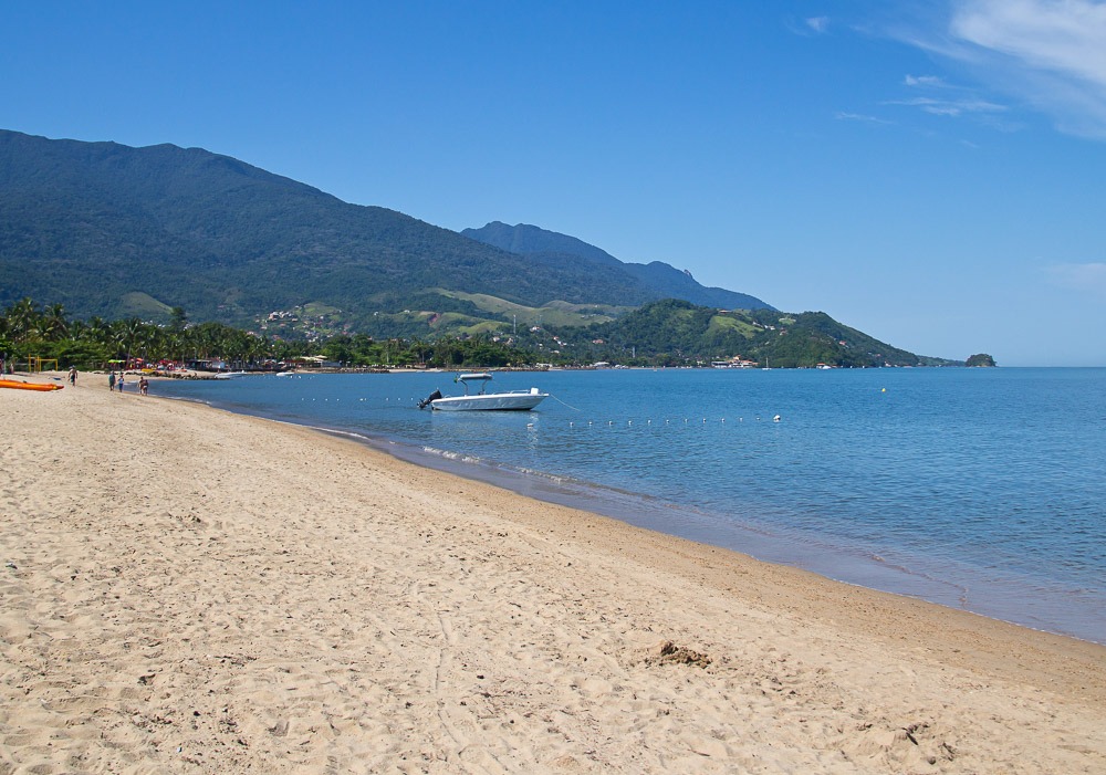 Praia do Perequê em Ilhabela com areia clara, mar calmo e barco ancorado.