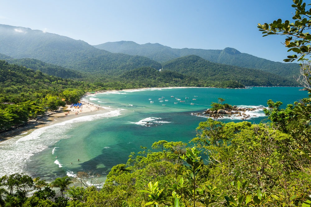 Vista panorâmica da Praia dos Castelhanos em Ilhabela, com mar azul e mata atlântica ao redor.