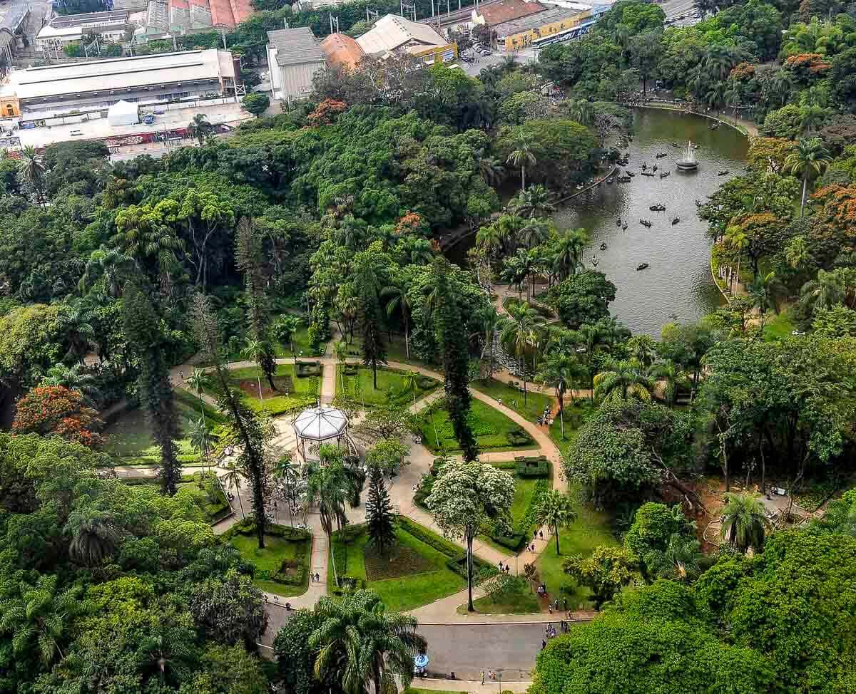 Vista aérea do Parque Municipal de Belo Horizonte com áreas verdes, lago e construções ao fundo.