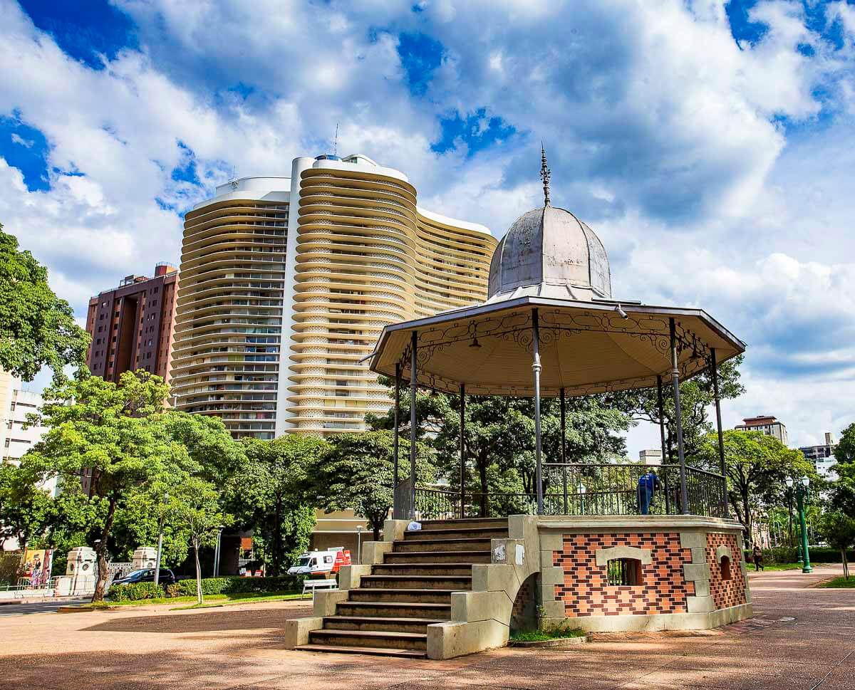 Coreto em praça arborizada na Savassi, com prédios altos e céu parcialmente nublado ao fundo.