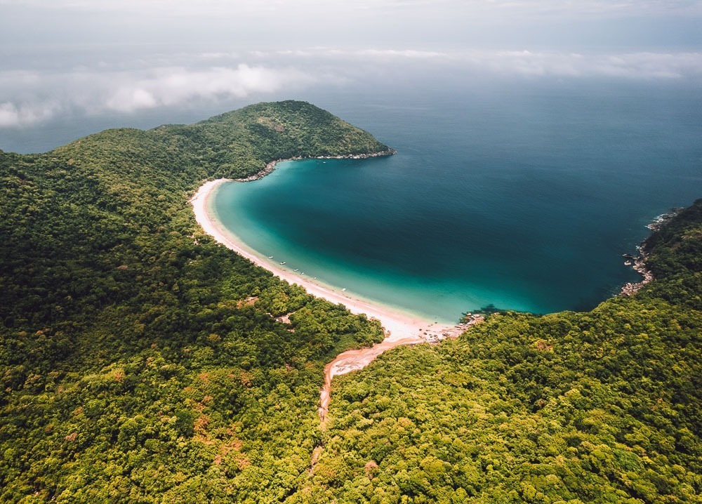 Vista aérea de parte da Ilha Grande, com mata densa ao redor e mar azul.