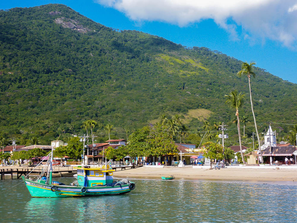 Praia da Vila do Abraão em Ilha Grande, com barco colorido na água e vila ao fundo.