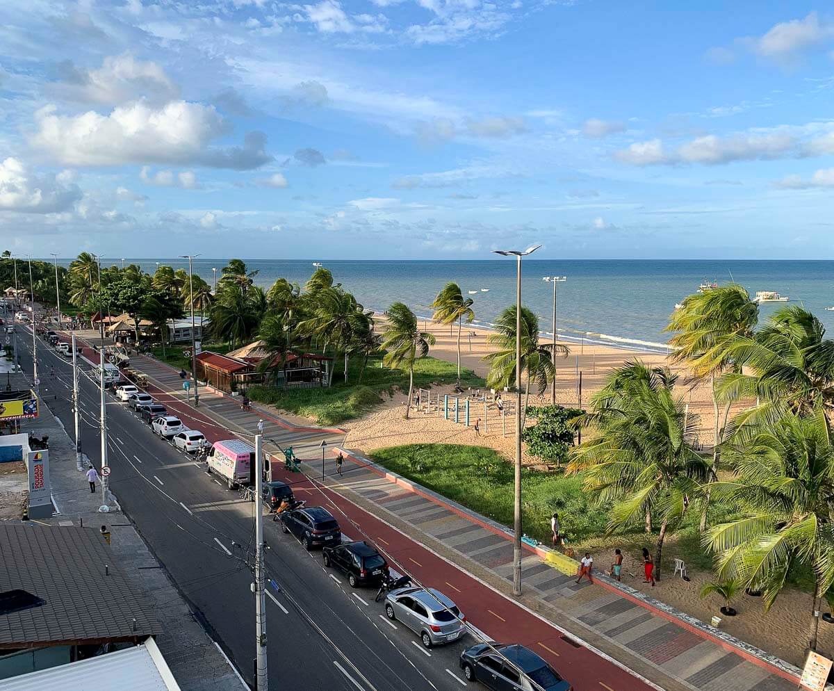 Calçadão de João Pessoa com ciclovia, coqueiros, faixa de areia clara e mar ao fundo.
