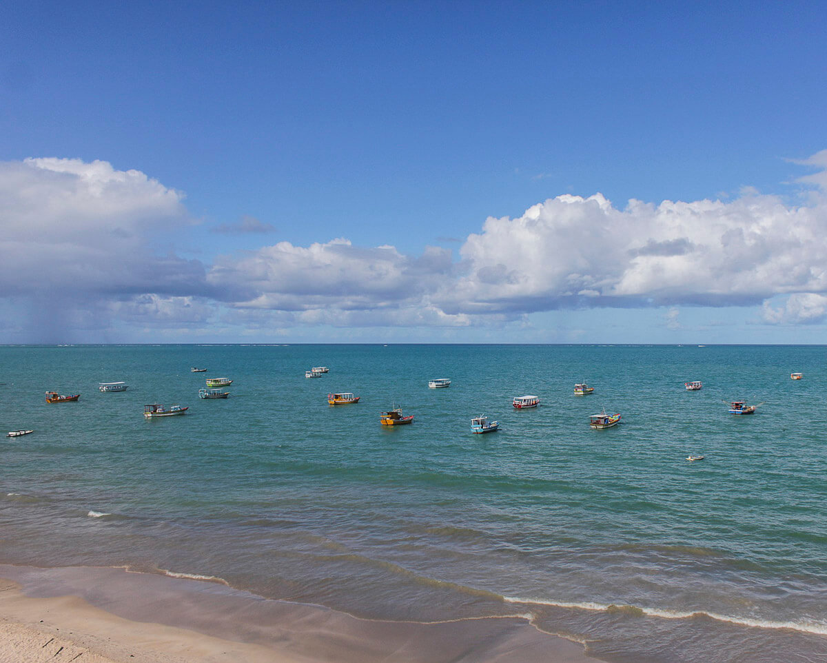 Mar azul-esverdeado repleto de pequenos barcos espalhados pela água sob um céu azul com nuvens densas.