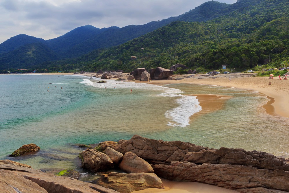 Praia do Cepilho, em Trindade, com ondas suaves, areia dourada e montanhas verdes ao fundo.