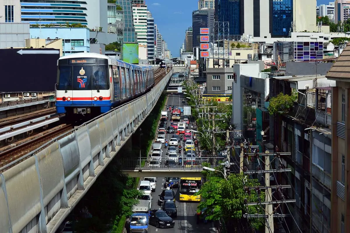 Trem do BTS Skytrain circula acima do trânsito intenso em Bangkok, rodeado por prédios modernos.