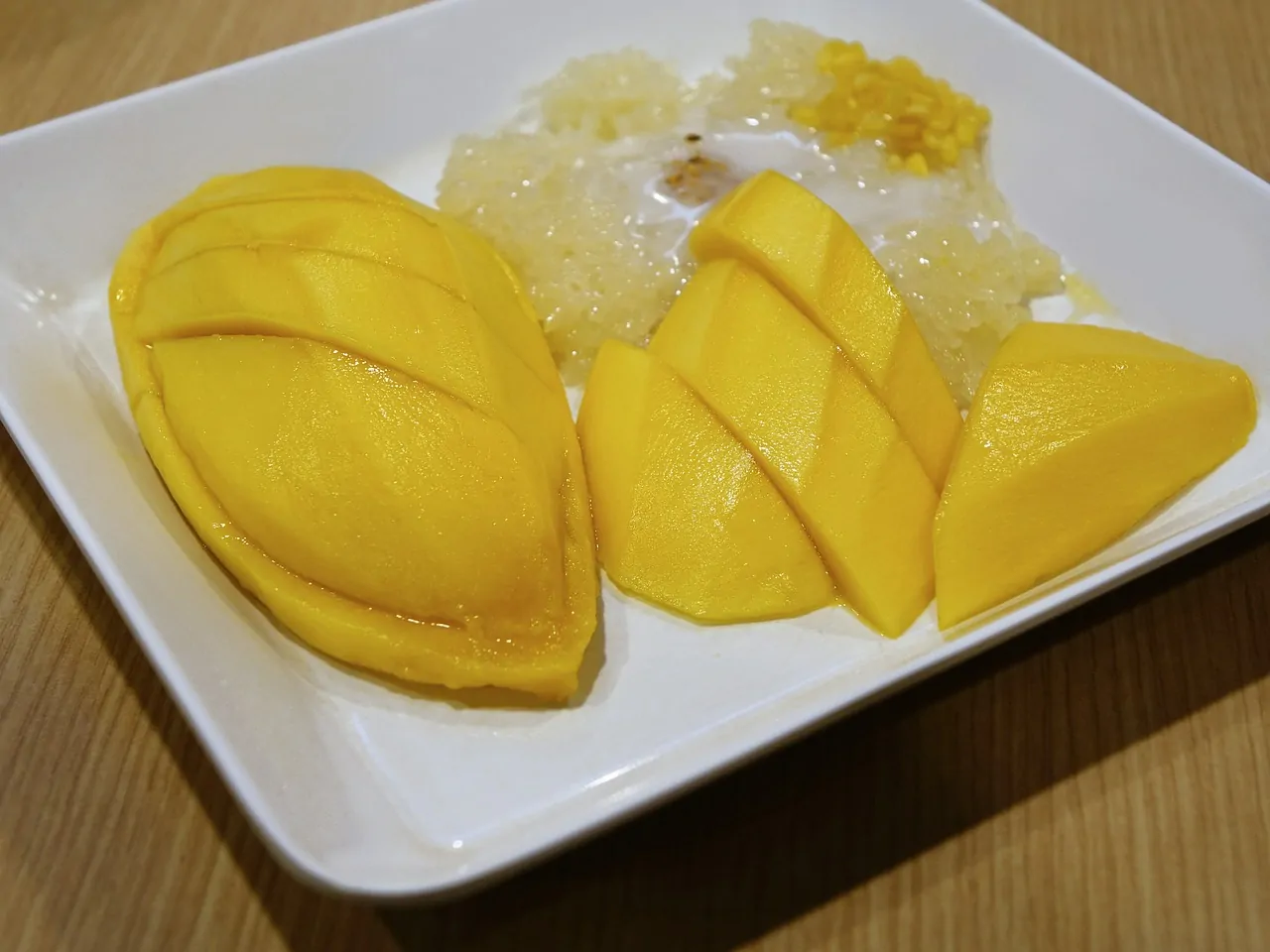 Prato tailandês com arroz doce e fatias de manga madura servidos em prato branco.