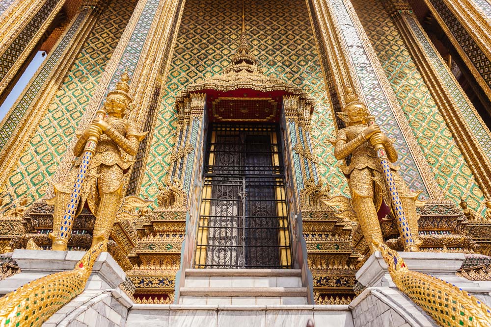 Entrada do Phra Mondop, no Grand Palace de Bangkok, com estátuas douradas de guardiões e decoração minuciosa nas paredes.