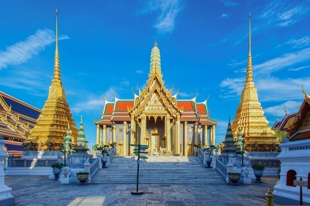 ntrada do templo Wat Phra Kaew com torres douradas e céu azul vibrante.