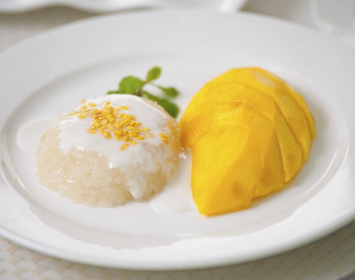 Prato típico tailandês com sticky rice coberto com leite de coco ao lado de fatias de manga madura.