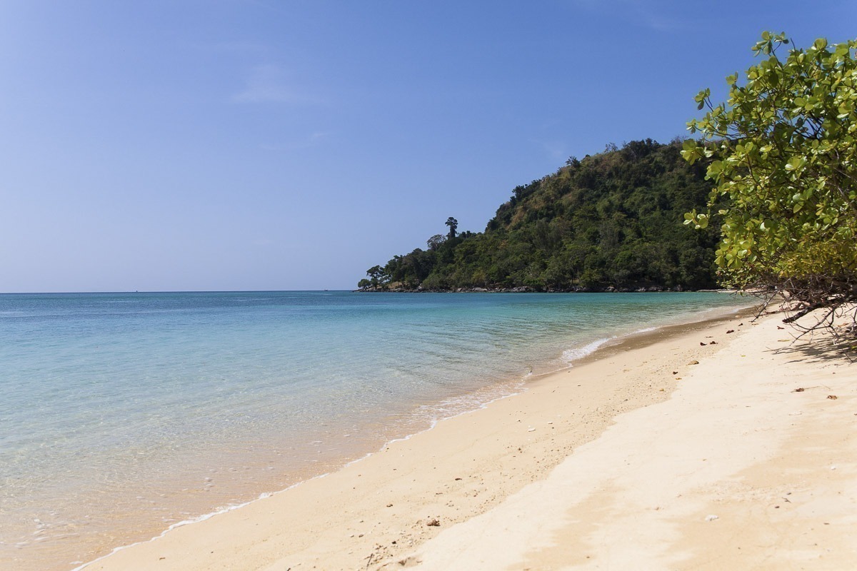 Praia em Koh Ngai com mar turquesa e floresta densa ao fundo.